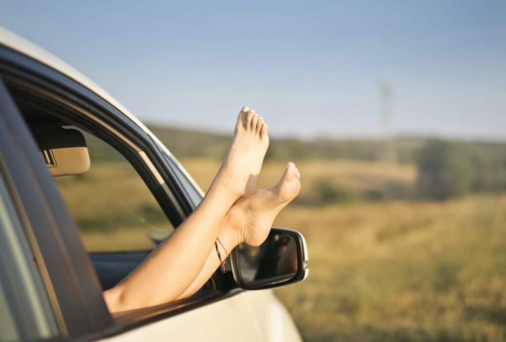 Crop carefree woman with legs sticking out of car window